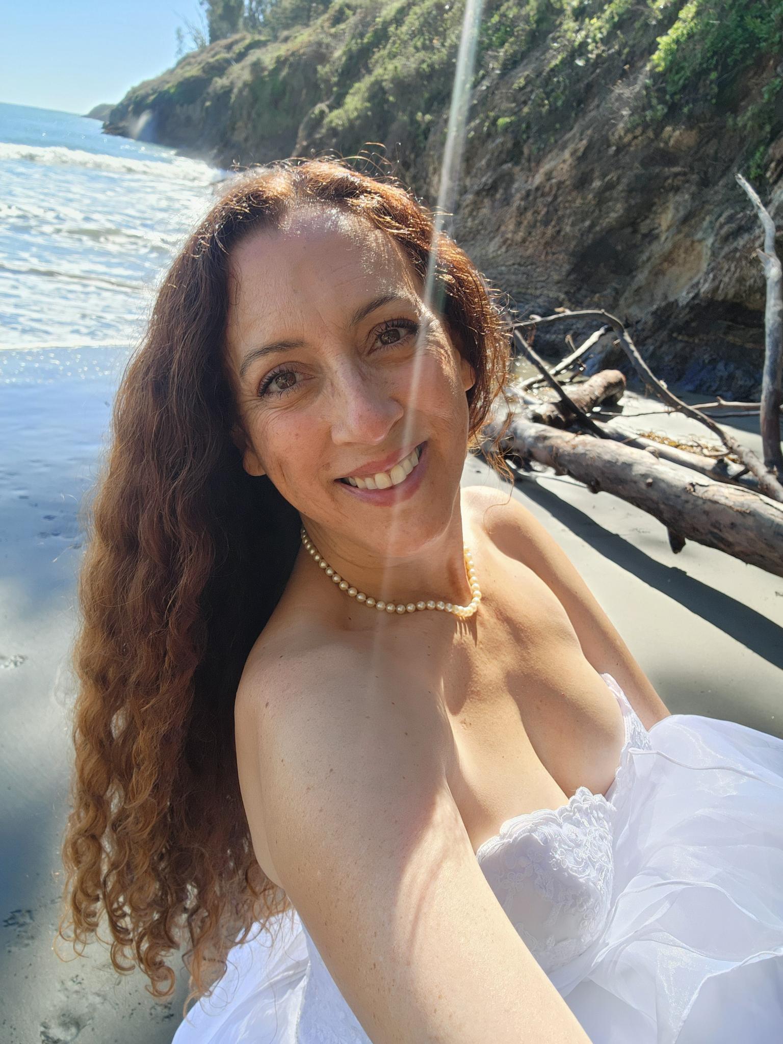 Andie smiling in her wedding dress in the sunlit cove