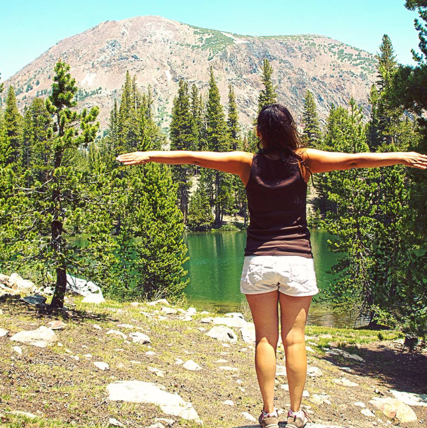 Andie with her arms outstretched above a mountain lake
