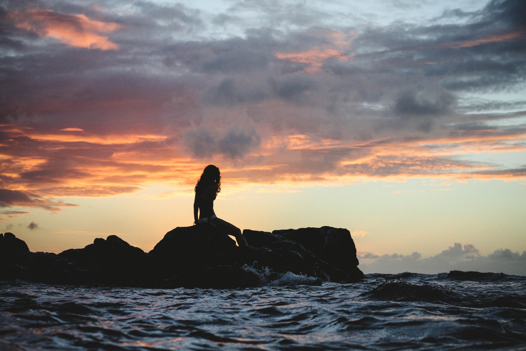 Ocean waves and a rocky shore beneath a glowing sunset