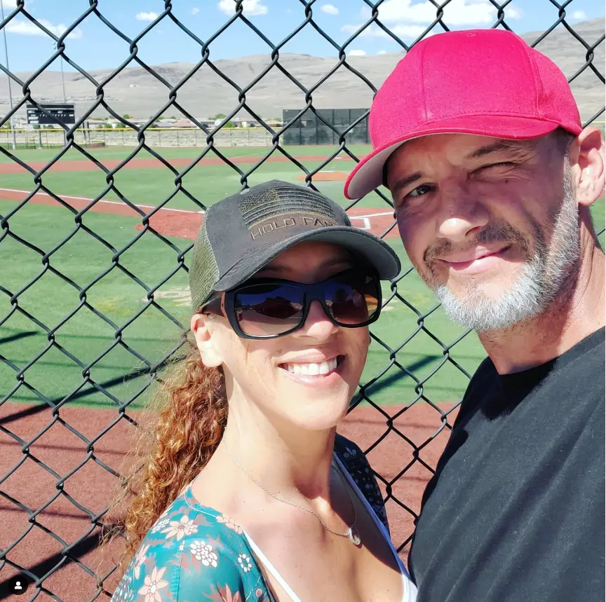 Andie and Greg smiling together at a baseball field